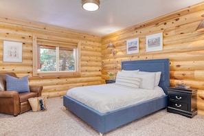 Relax in this serene bedroom with a large bed, comfortable sofa, and a window offering a view of the surrounding trees.