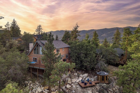A cabin with a deck, surrounded by trees and mountains.