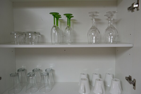 Une étagère blanche sur laquelle sont disposés divers objets en verre, notamment des verres à vin et des verres à cocktail.