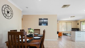 Un coin repas avec une table en bois dressée pour quatre personnes, une horloge au mur et un tableau représentant un paysage urbain au-dessus de la table.