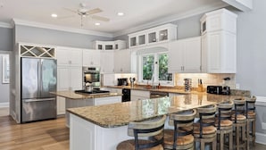 A modern kitchen with white cabinetry, a stainless steel refrigerator, granite countertops, and a central island with bar stools. - Hilton Ivory 15th Hole of Harbourtown Golf Course Private Pool + Hot Tub (Hilton Head Island)