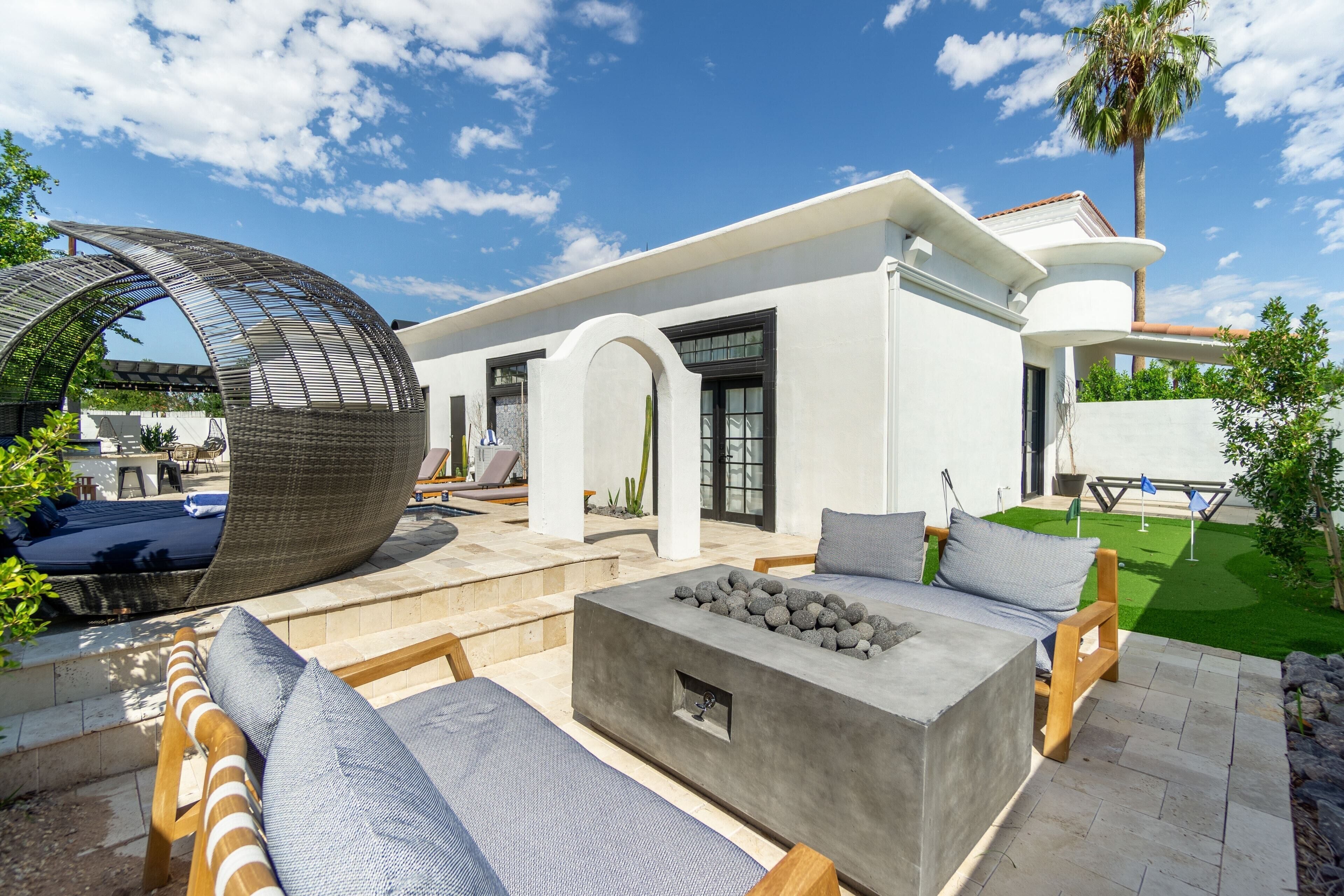 A modern outdoor patio with a fire pit, lounge chairs, and a unique curved glass structure.