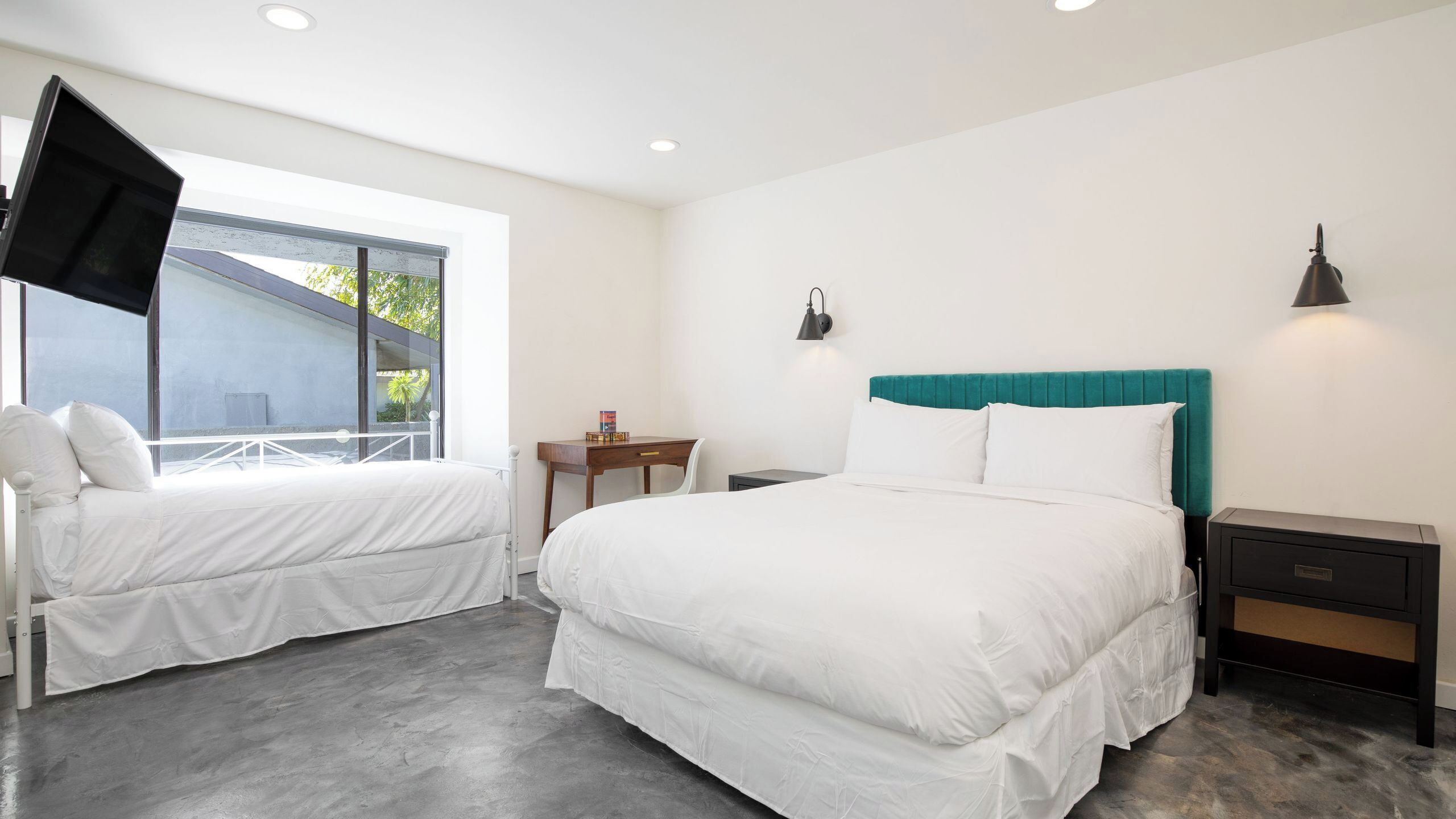 A hotel room with two beds, a desk, a chair, a TV, and a window with a view.