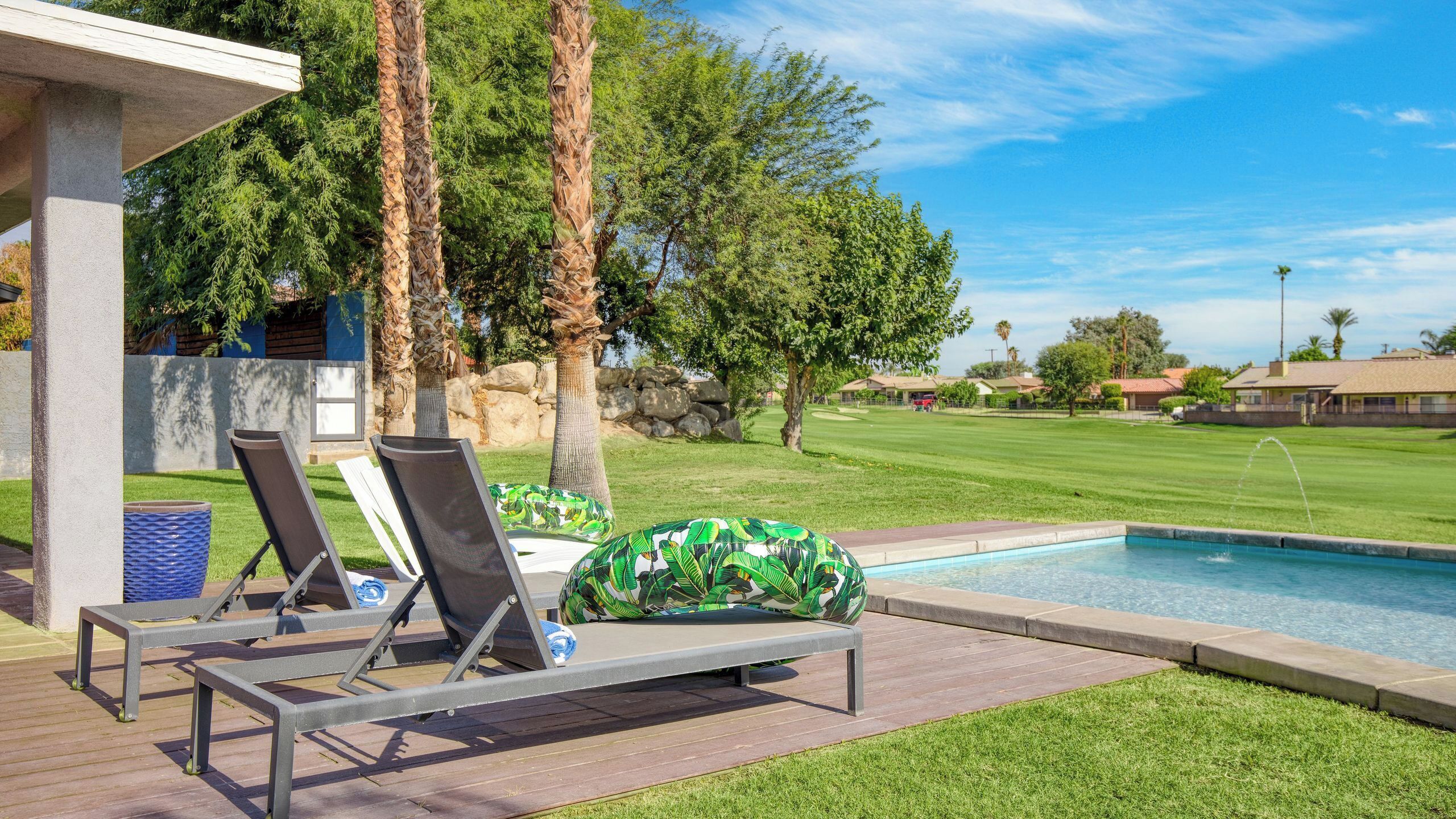 Ein Poolbereich mit Liegestühlen, einem kleinen Tisch und Blick auf einen Golfplatz.