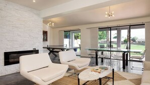 A modern living room with a fireplace, a ping pong table, and a dining area with chairs and a glass table.