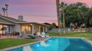 A modern house with a swimming pool, outdoor seating, and a stone wall.