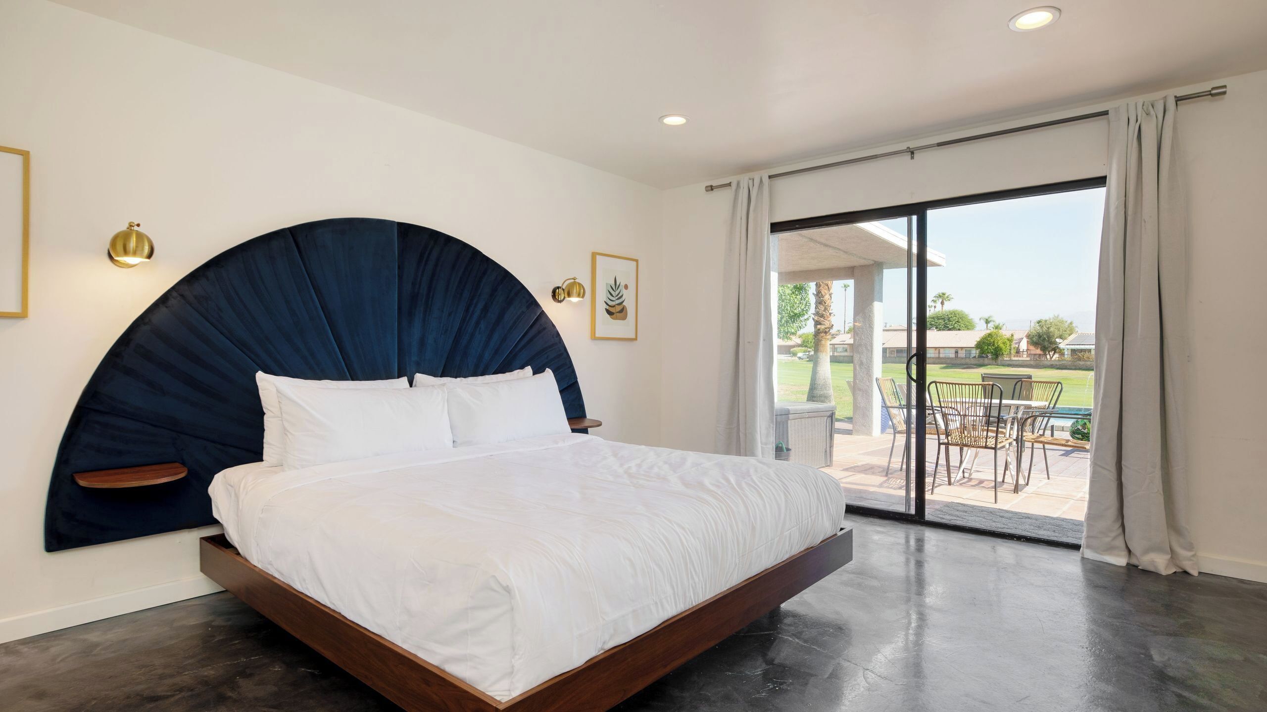 A modern bedroom with a curved headboard, a large bed, and a sliding glass door leading to an outdoor patio.