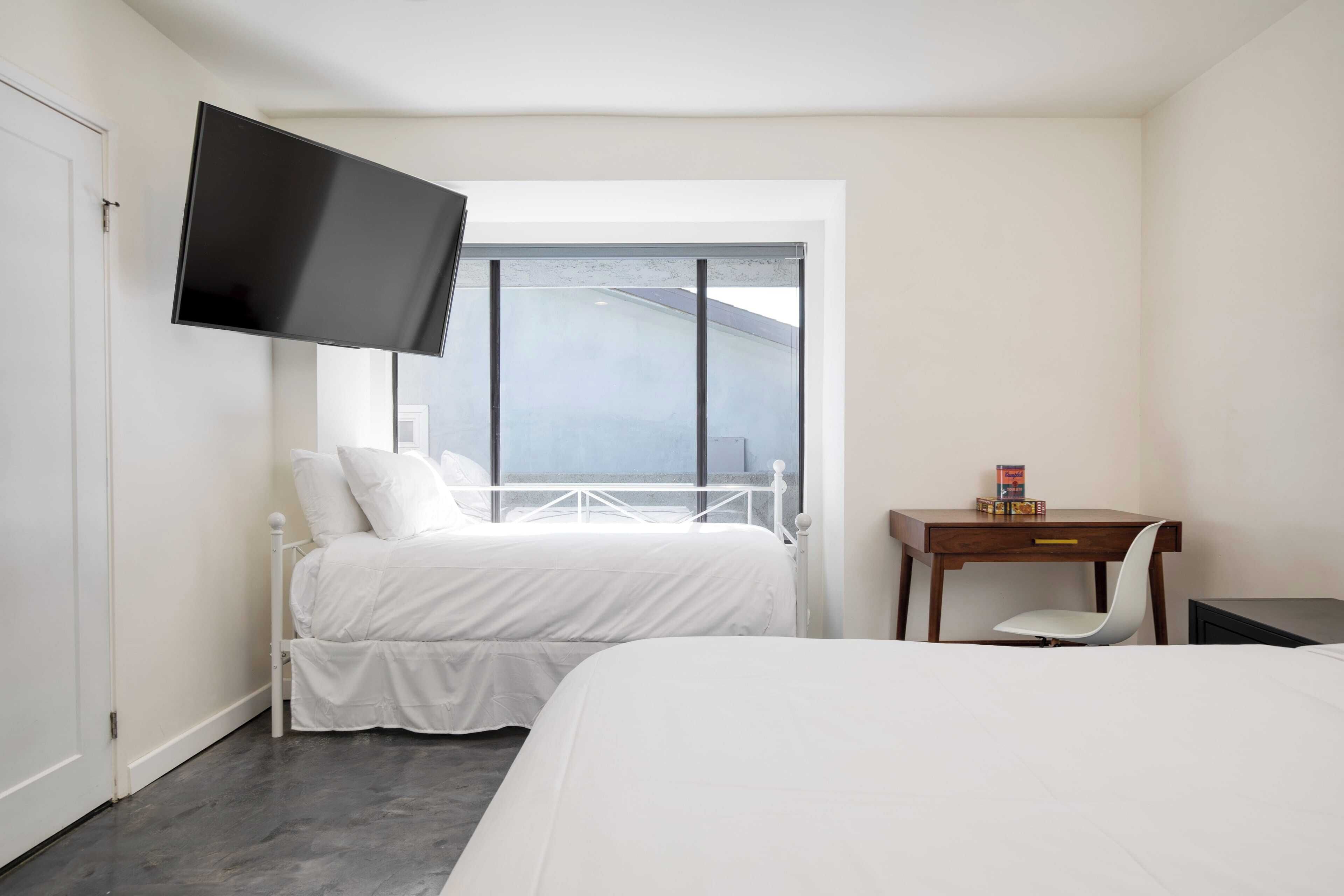 Une chambre d’hôtel équipée d’un lit, d’un bureau, d’une chaise, d’une télévision et d’une fenêtre donnant sur le ciel.