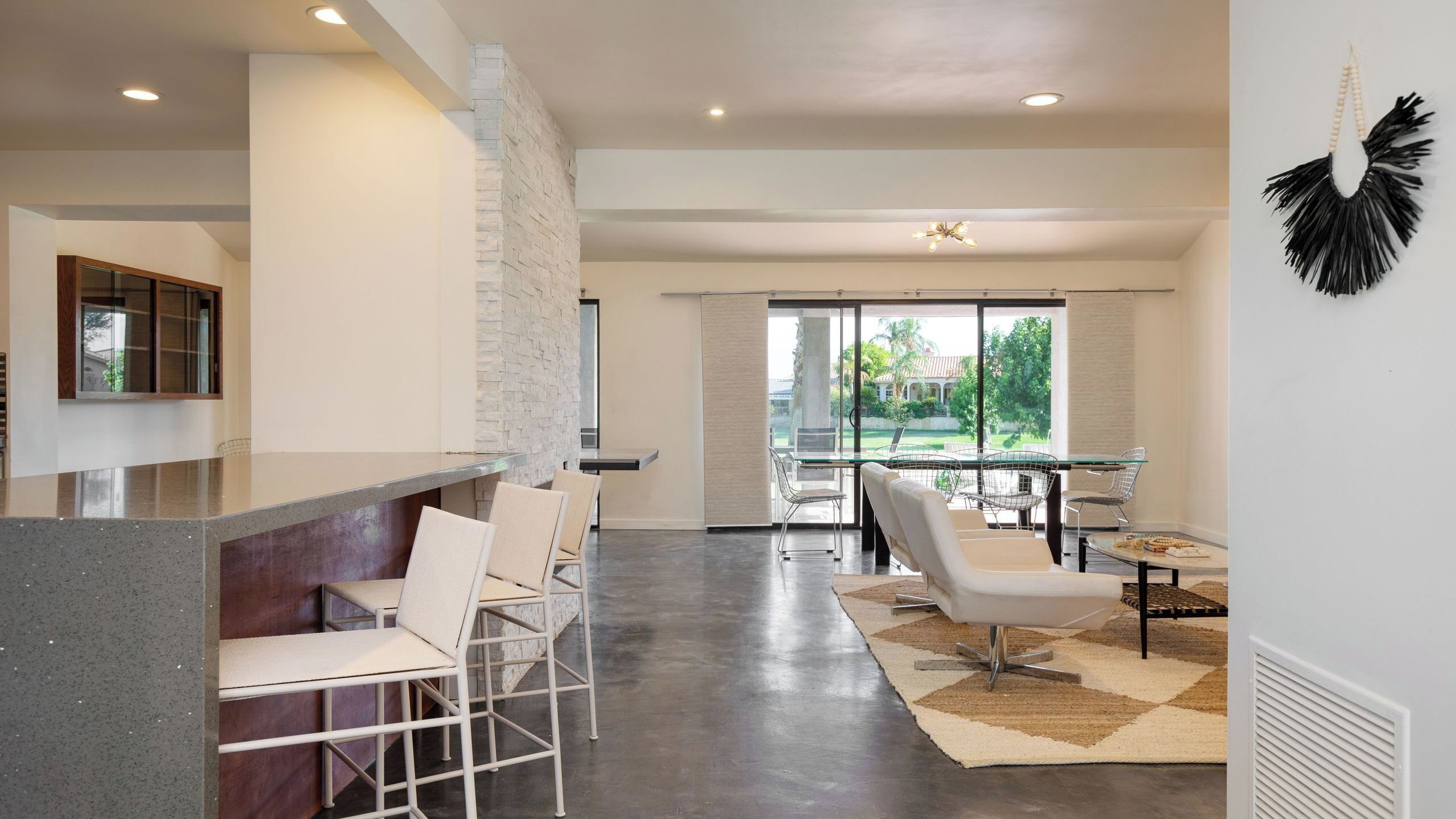 A modern kitchen with a stone accent wall, a dining area with a glass table and chairs, and a view of a garden.