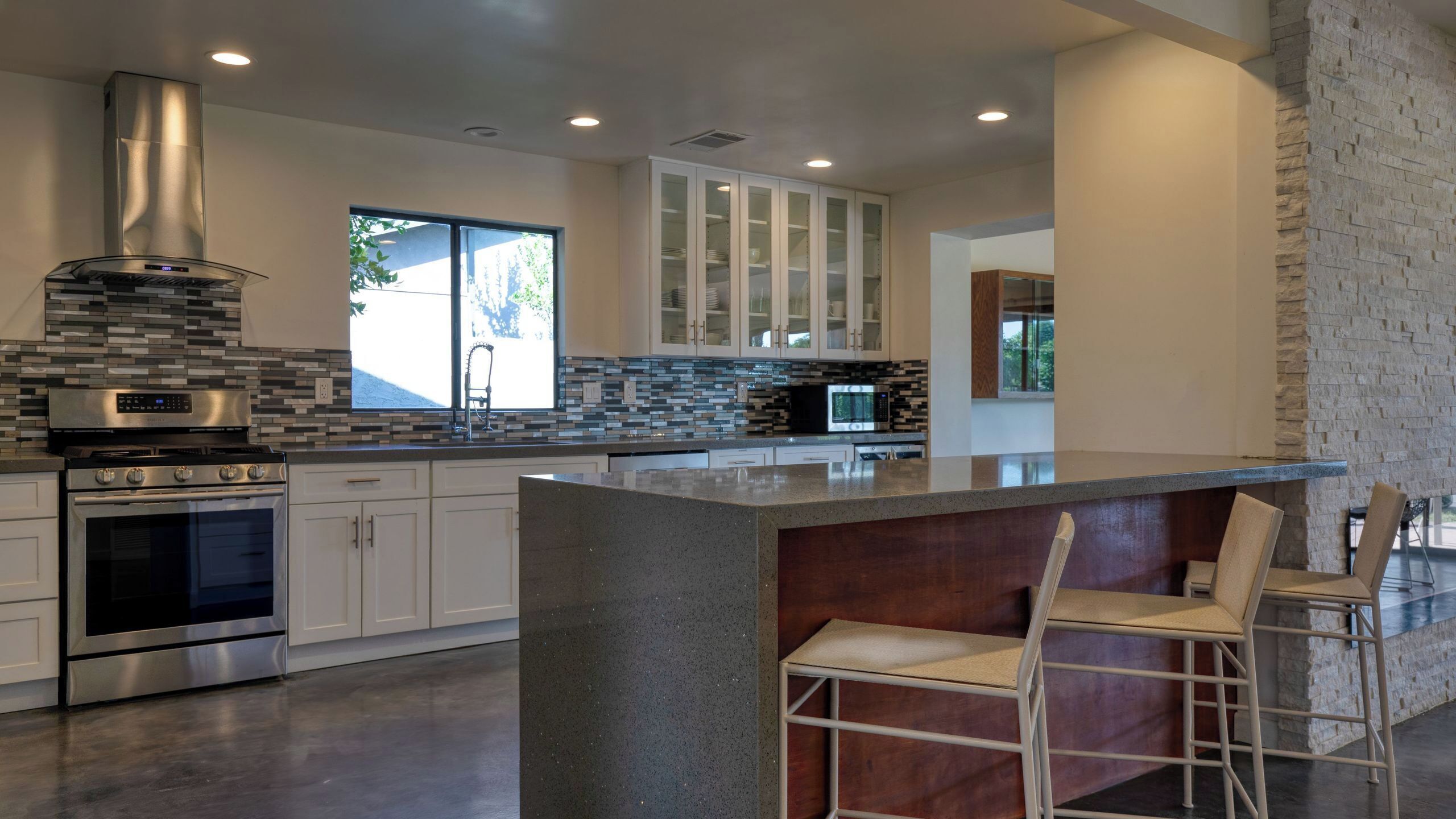 A modern kitchen with a central island, stainless steel appliances, and a view to the outdoors.