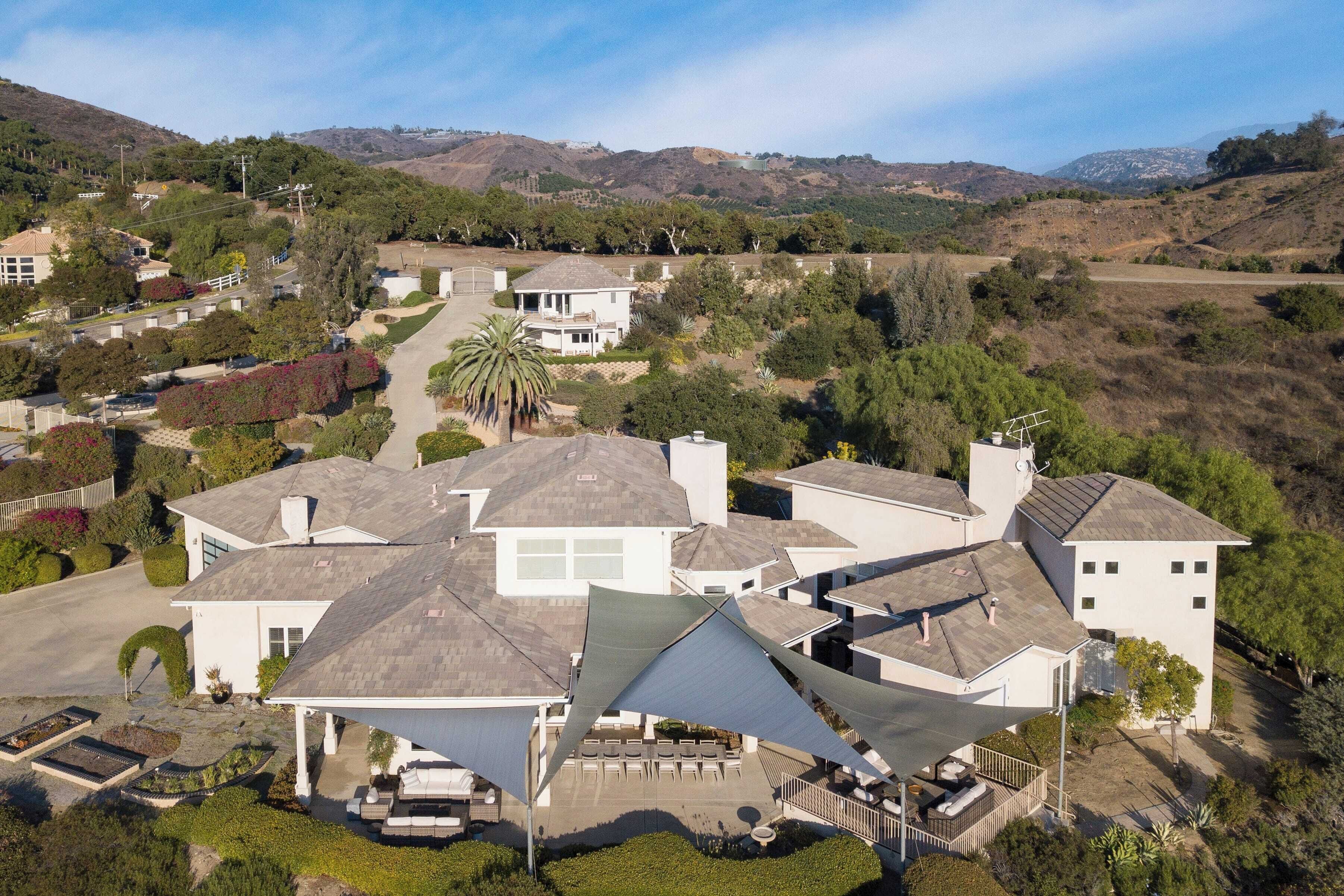 A residential area with multiple houses, a driveway, and a hilly landscape in the background.