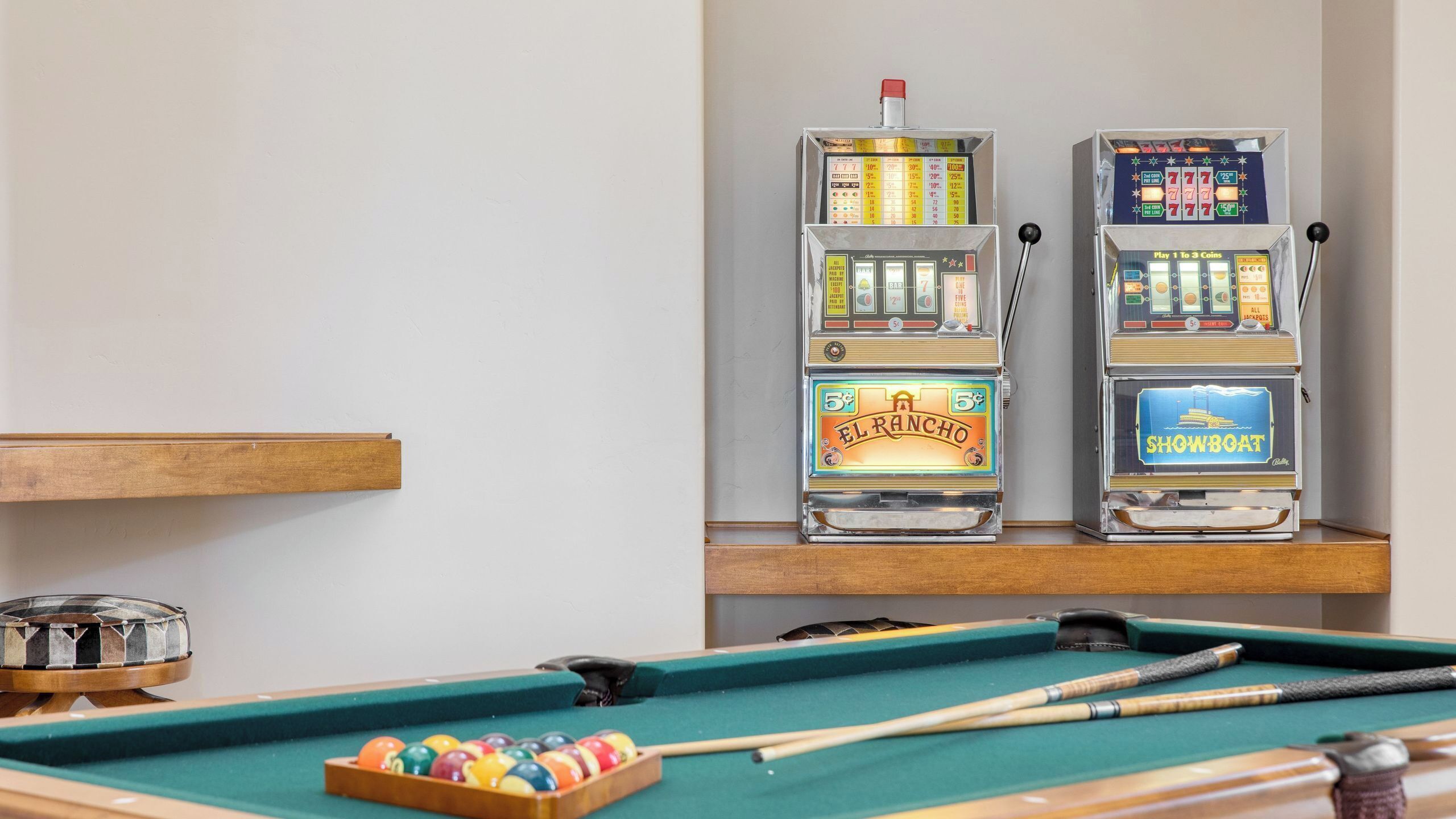 A pool table with two slot machines, a pool cue, and a set of balls.