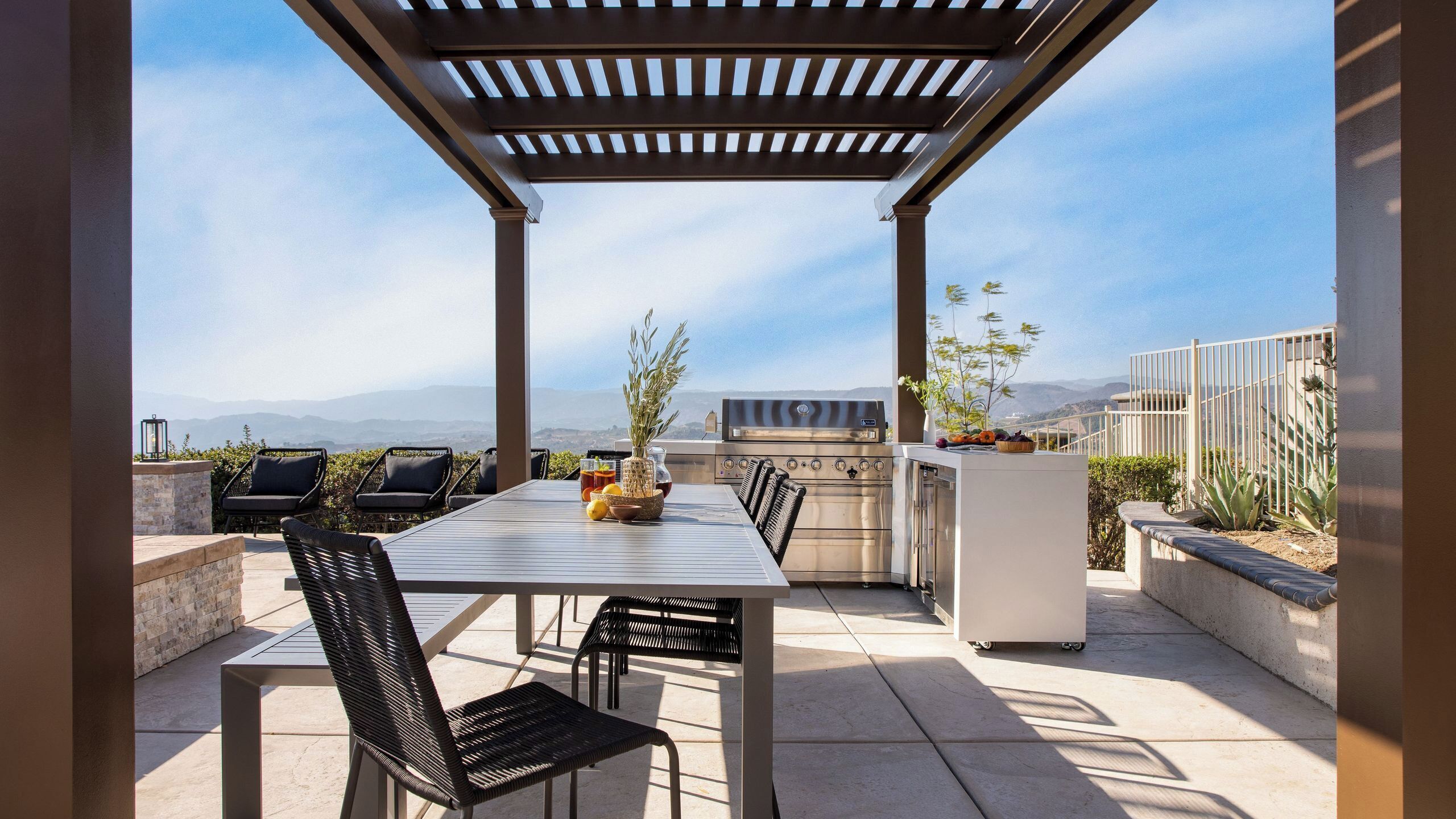 An outdoor patio with a pergola, a grill, and a dining table with chairs.