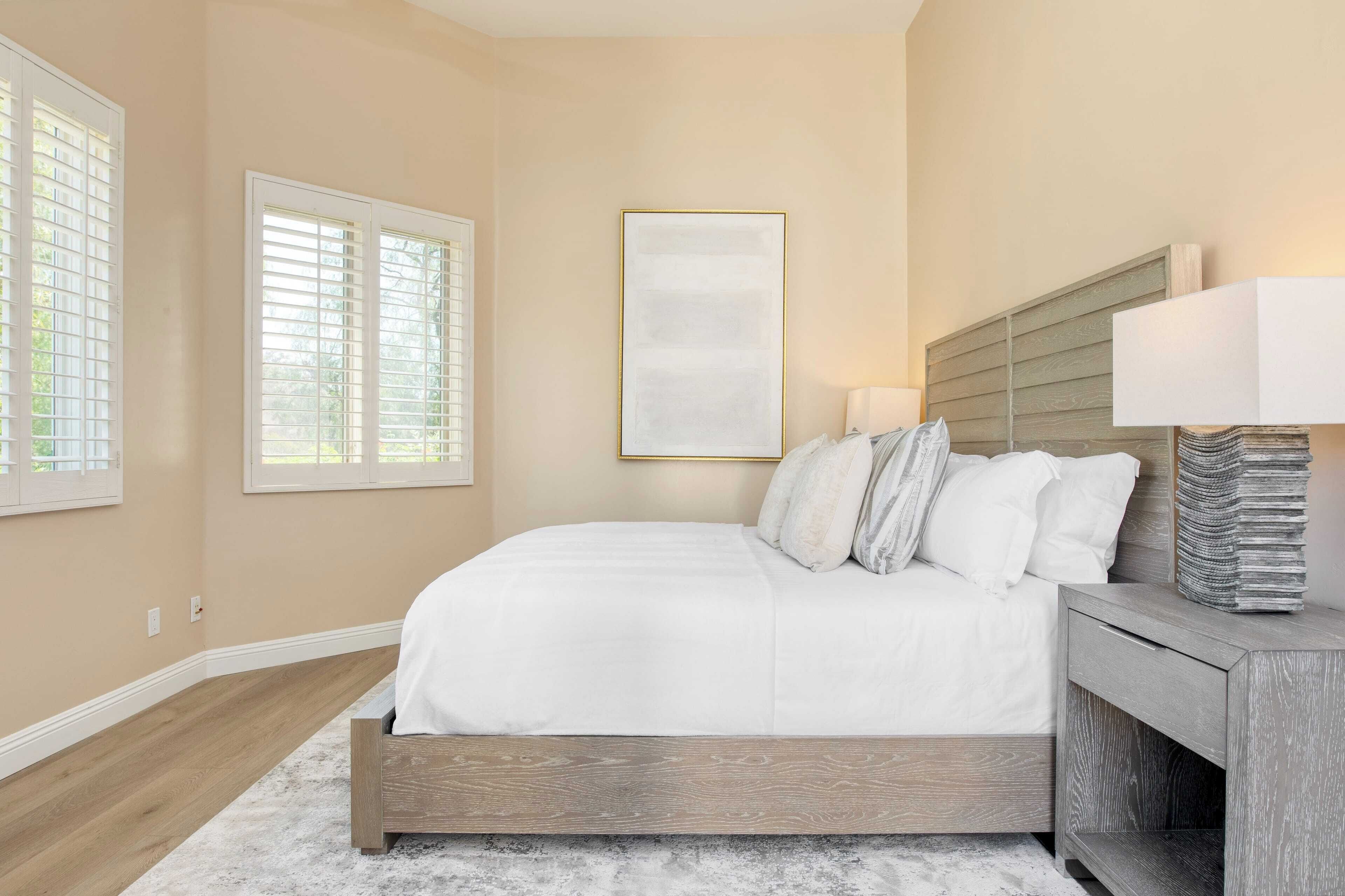A bedroom with a bed, bedside table, lamp, and a framed artwork on the wall.