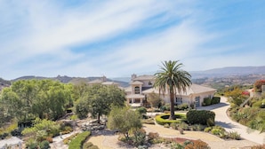 Un'ampia casa con giardino, una palma e vista sulle colline.