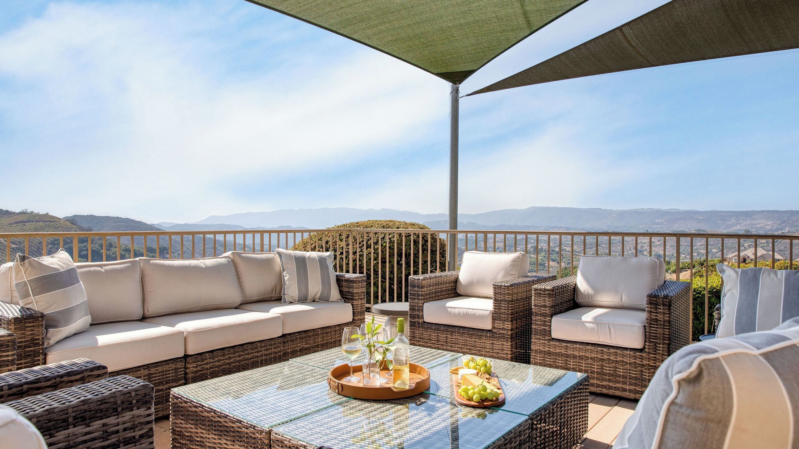 A terrace with wicker furniture, a glass table, and a view of distant hills.