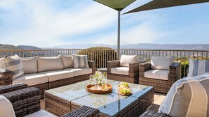 Eine Terrasse mit Korbmöbeln, einem Glastisch und Blick auf ferne Hügel.