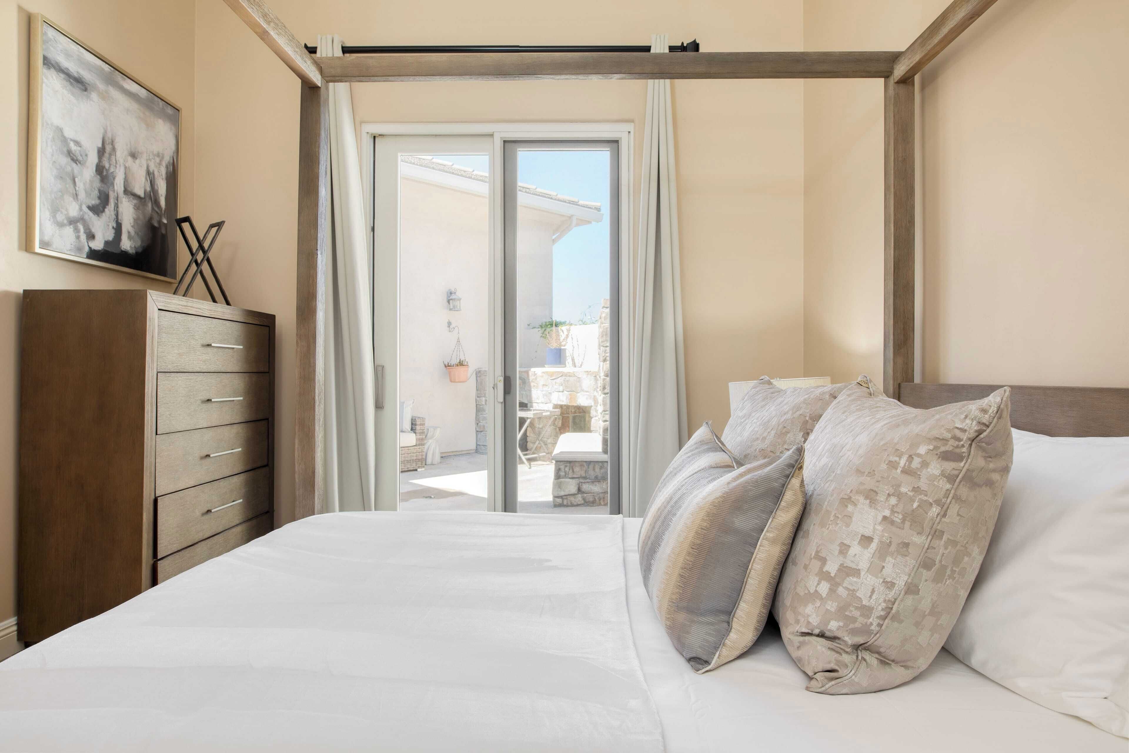 Ein Schlafzimmer mit einem Bett, einer hölzernen Kommode und Blick auf die Terrasse durch eine Schiebetür.