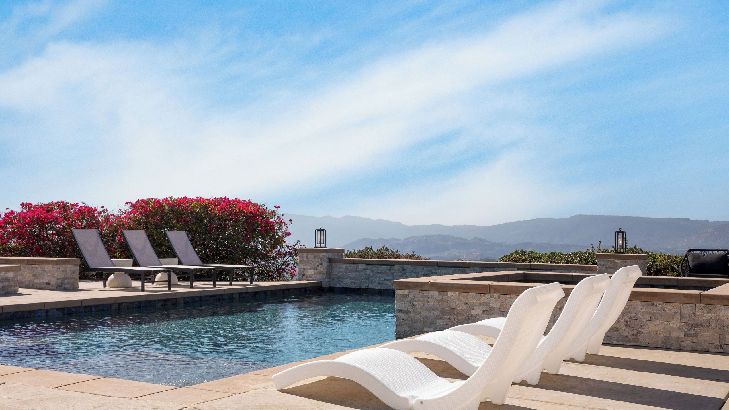 A pool area with lounge chairs, a view of mountains, and a clear sky.