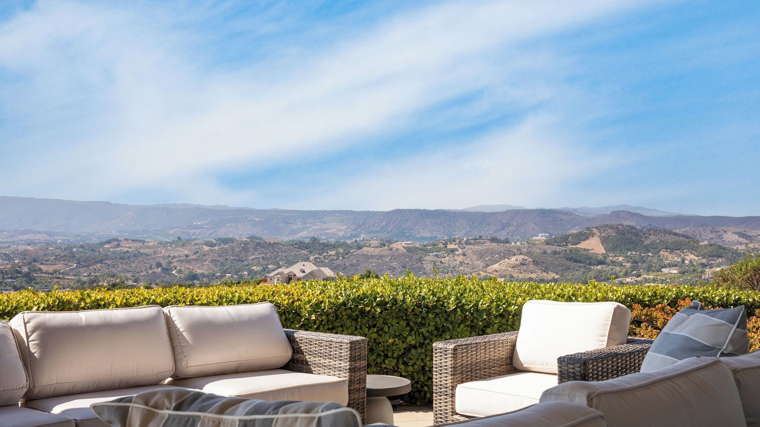 A patio with wicker furniture and a view of a hilly landscape.