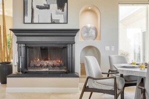 A modern living room with a fireplace, a dining area with chairs, and a large abstract painting on the wall.