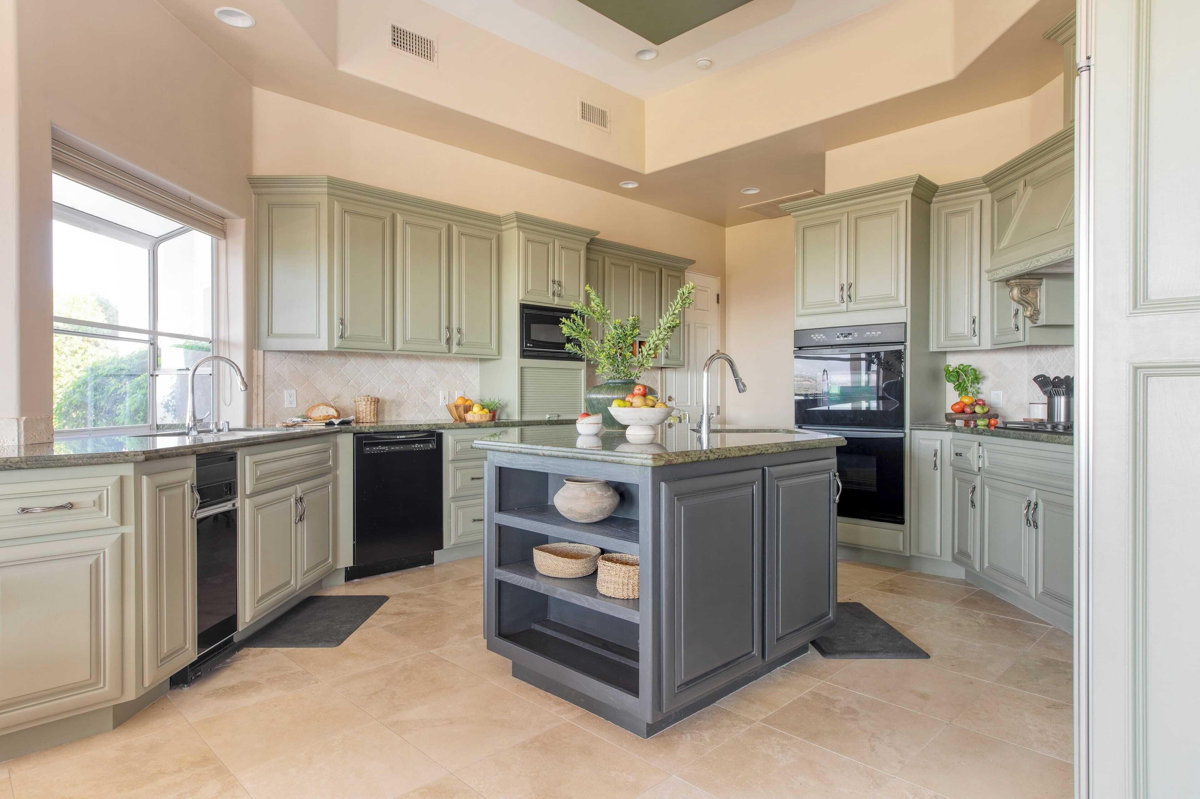 A kitchen with light green cabinets, a central island with a sink, and a window providing natural light.