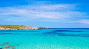 Un paisaje costero con aguas turquesas cristalinas, una costa rocosa y una masa de tierra en la distancia.