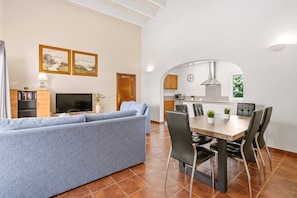 Een moderne woonkamer met een bank, een eettafel met stoelen, een televisie en ingelijste foto's aan de muur.