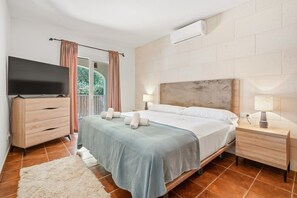A bedroom with a bed, a TV, a dresser, a nightstand, and an air conditioning unit.