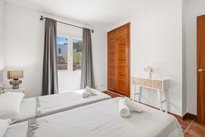 Habitación de hotel con dos camas, un armario de madera, una mesita de noche con lámpara y vistas al exterior.