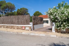Una entrada protegida por un muro de piedra, un edificio con techo de tejas rojas y un arbusto floreciente.