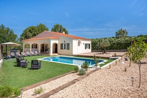 A villa with a swimming pool, outdoor seating, and a garden.
