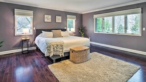 A bedroom with a large bed, two bedside tables, a nightstand, a woven basket, and a large window with a view of trees. - Spacious Rochester Home w/ Heated Pool & Hot Tub! (Rochester)