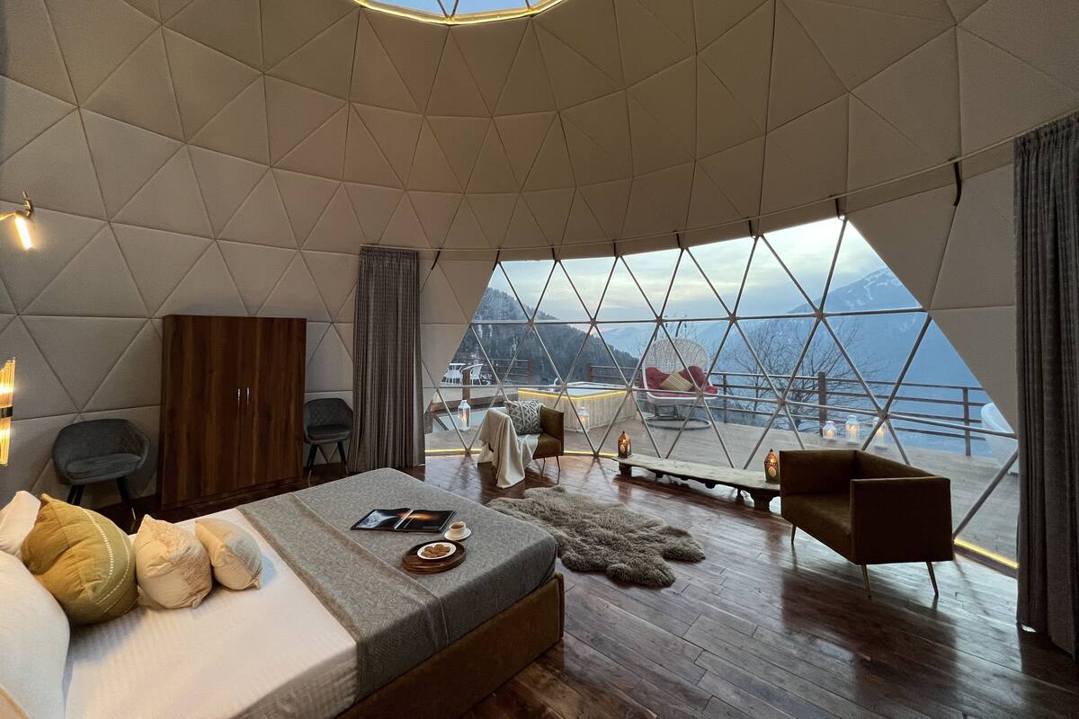 A modern, spacious room with a large bed, a wooden wardrobe, and a view of a mountainous landscape through a large window.