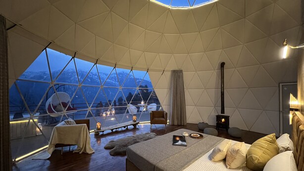 A spacious room with a large bed, a wooden floor, and a view of mountains through a geometric window. - GLAMPING CLUB (Manali)