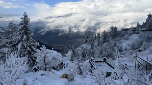 A snowy landscape with a mountain in the background, a clear sky, and a few buildings partially covered in snow. - GLAMPING CLUB (Manali)
