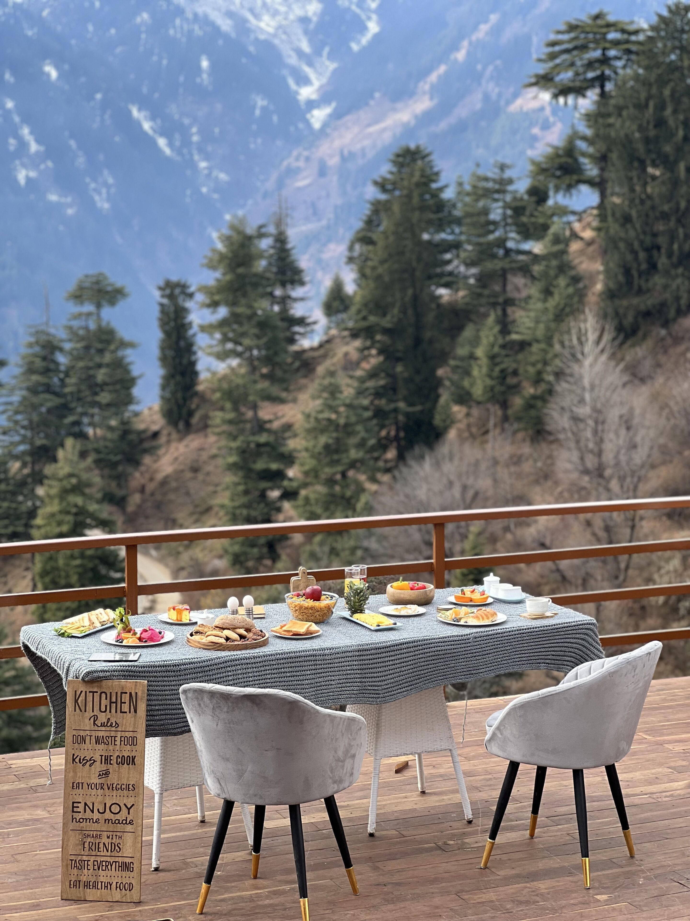 Ein Esstisch auf einer Terrasse mit Blick auf die Berge, umgeben von Stühlen.