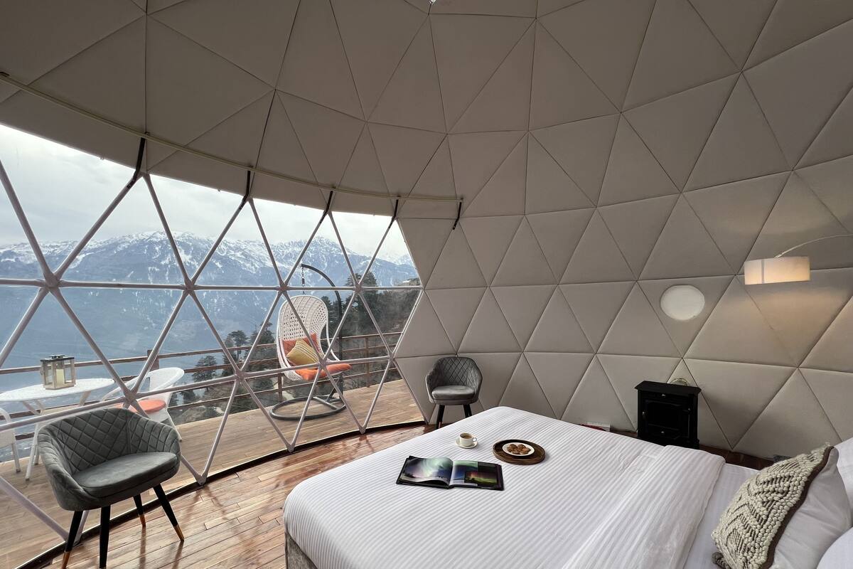 A modern, geometric interior with a bed, seating area, and a view of snow-capped mountains.