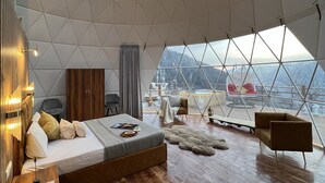 A spacious room with a large skylight, wooden flooring, a bed, seating area, and a view of the outdoors. - GLAMPING CLUB (Manali)