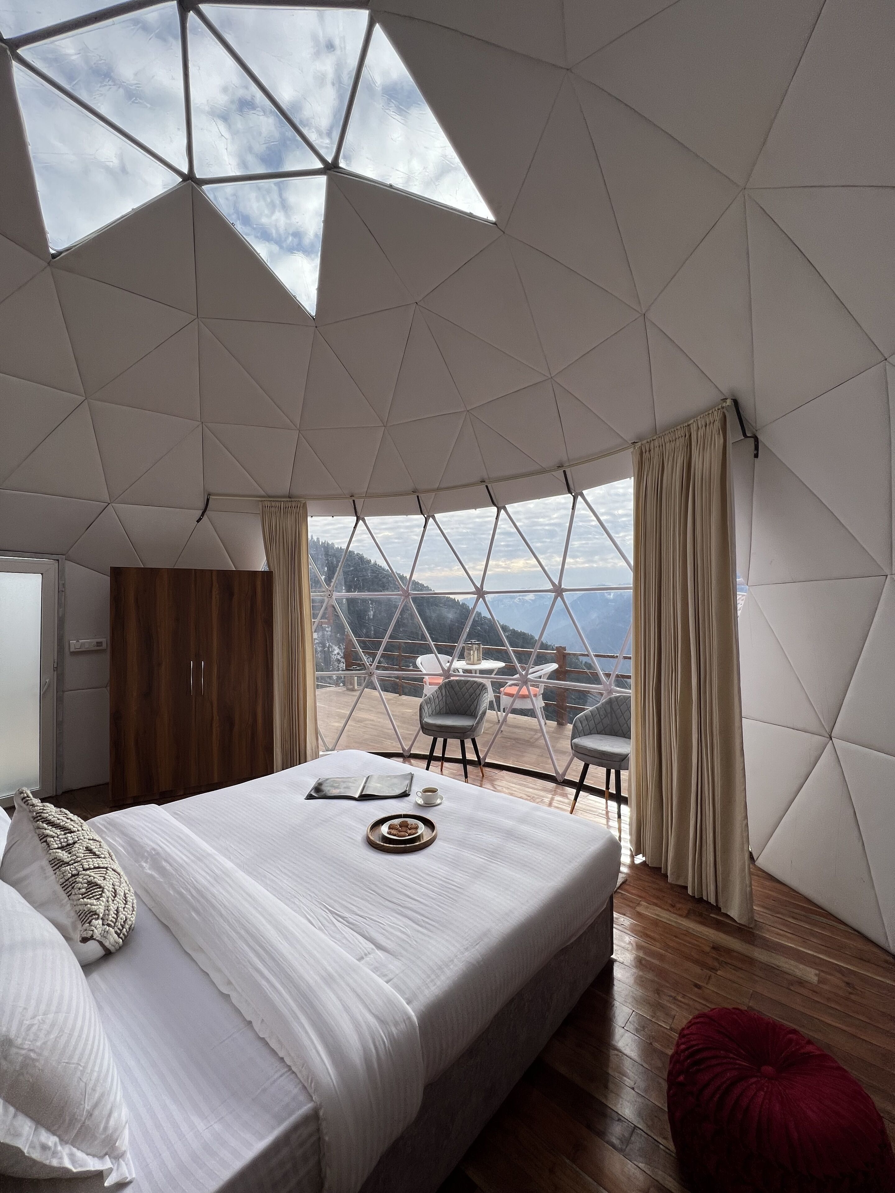 Un dormitorio con una cama grande, un armario de madera y vistas al exterior a través de un techo geométrico.