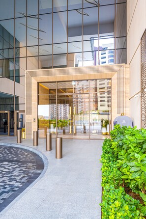 A modern building entrance with glass doors, a tiled floor, and a green hedge. - Ultra Luxury Palm Tower with Shared Hotel Facilities (Dubai)