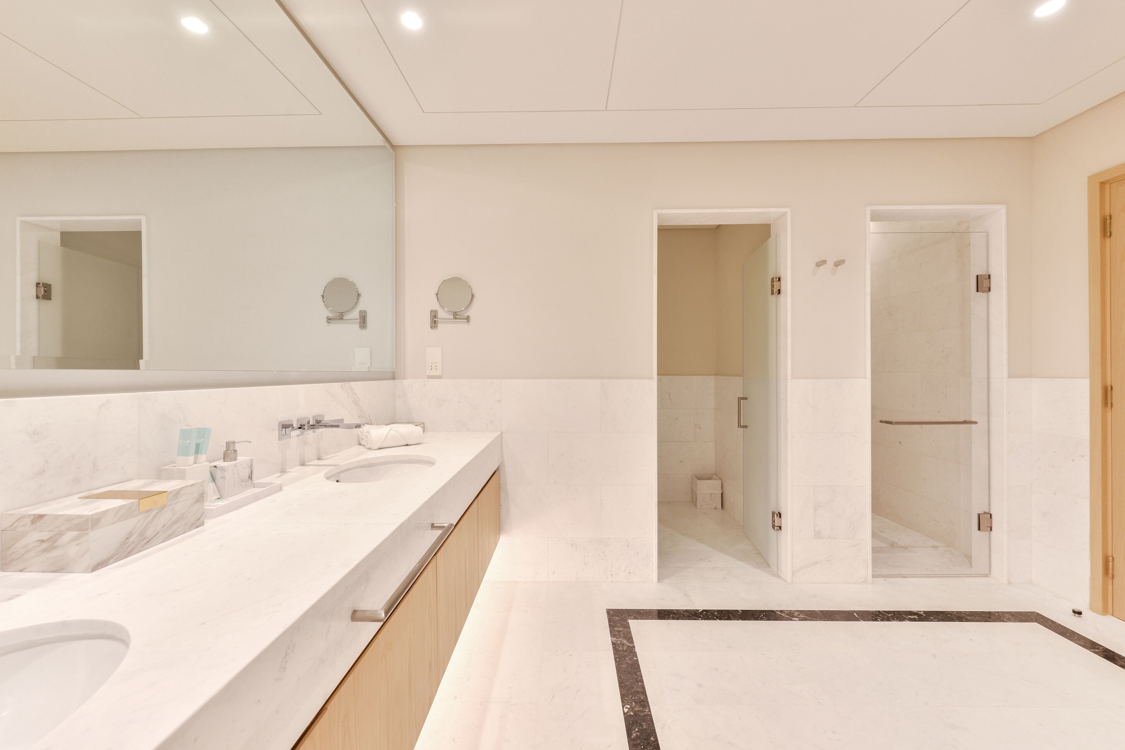 Une salle de bain moderne dotée d’un grand meuble-lavabo, de deux vasques, d’un miroir et d’un espace douche.