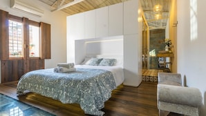 Ein modernes Schlafzimmer mit einem großen Bett, einem Einbauschrank und Blick auf die Küche durch eine Glastür.