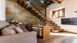 Ein modernes Wohnzimmer mit Steinwand, Holztreppe, grauem Sofa und Flachbildfernseher.