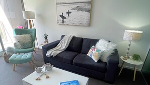 A living room with a dark blue sofa, a white coffee table, a teal armchair, and a painting of birds on the wall.