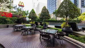 An outdoor seating area with tables and chairs, surrounded by greenery and urban buildings. - ★StayHere★ 1 Bedroom Avant Fort Bonifacio BGC (Taguig)