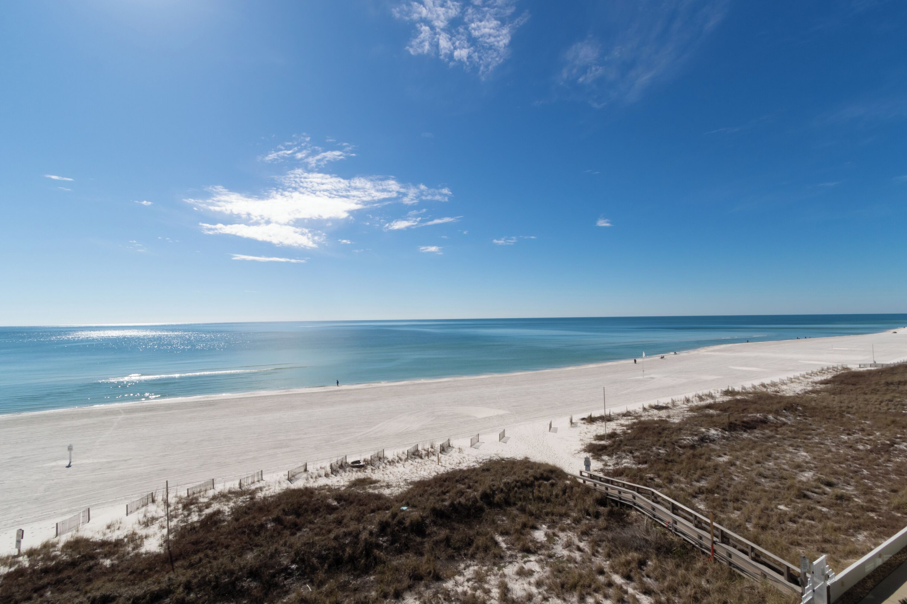 A beach with a sandy shore, a wooden walkway, and a clear blue sky.