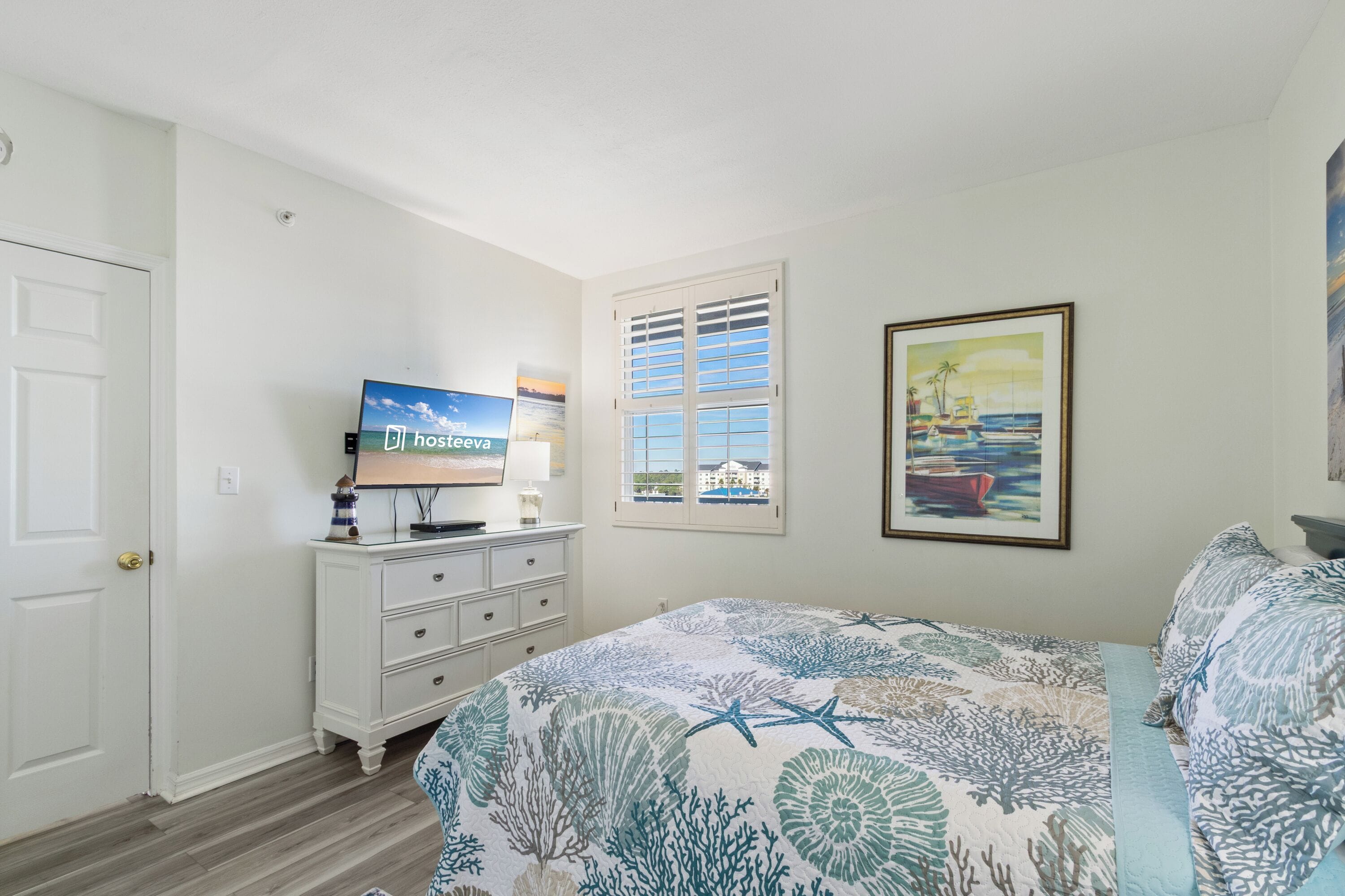 A bedroom with a bed, a dresser, a television, a window with blinds, and a framed picture on the wall.