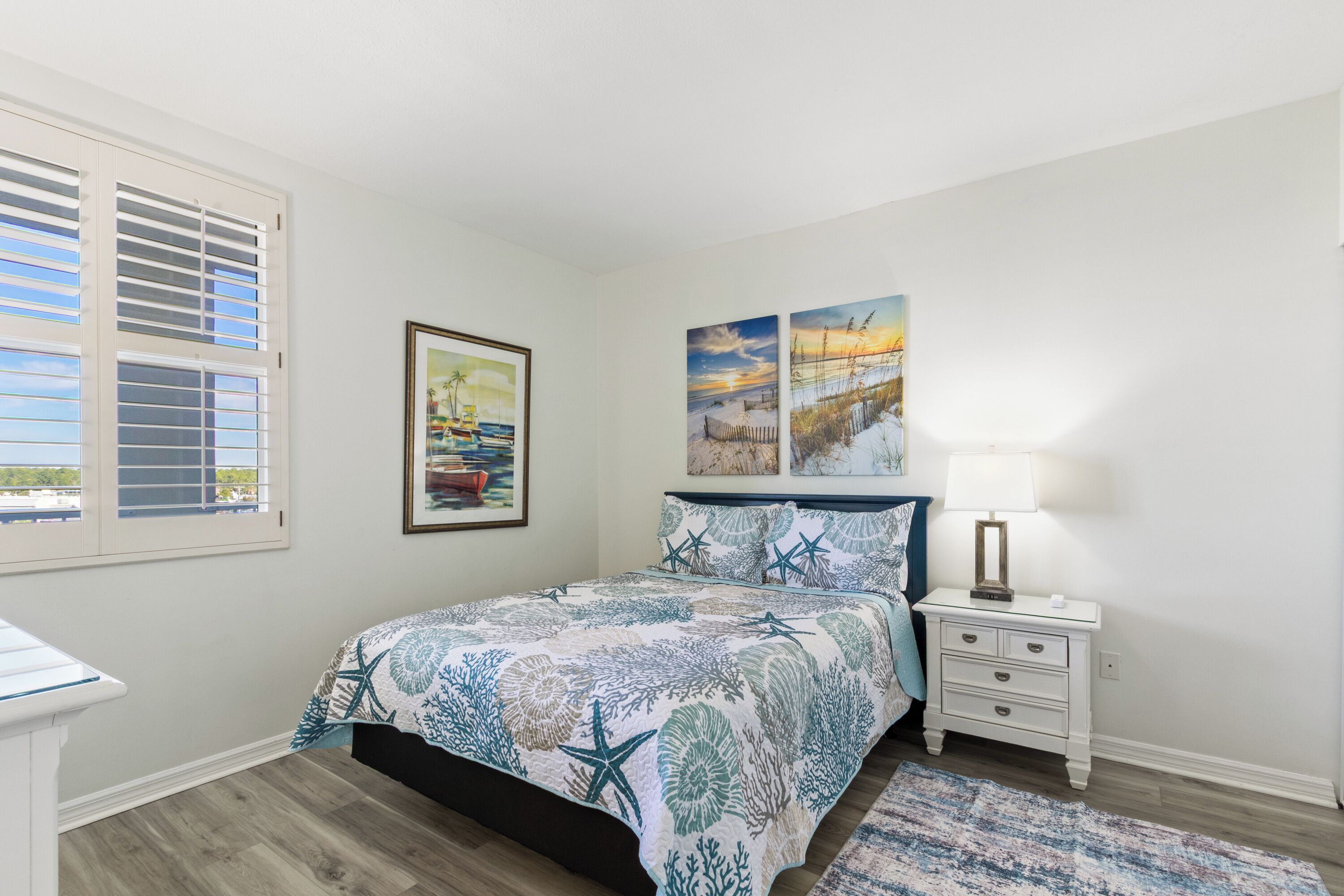 A bedroom with a bed, a nightstand, a lamp, and two wall-mounted paintings.