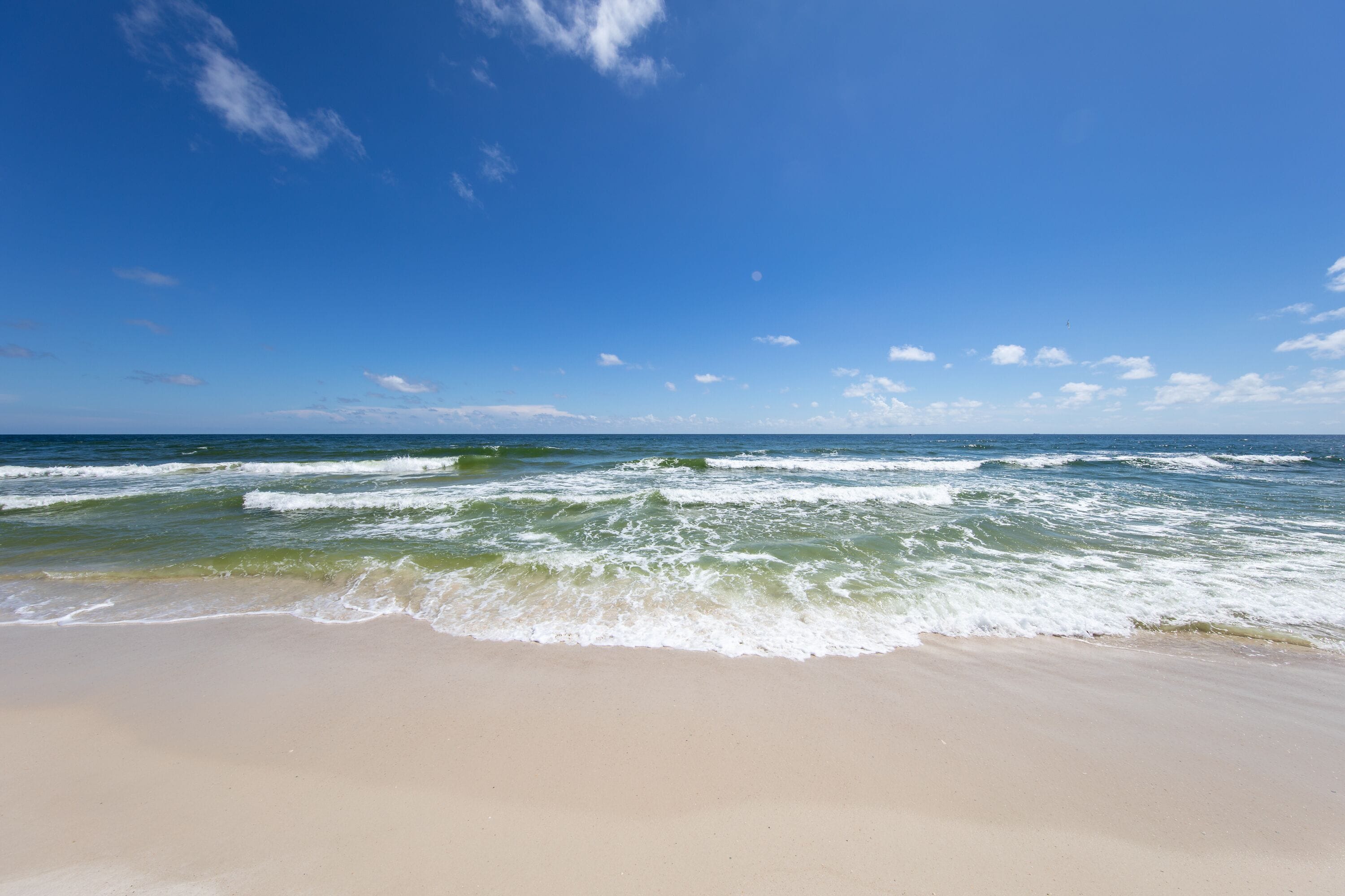 Ein Strand mit Wellen, blauem Himmel und weiter Ferne.